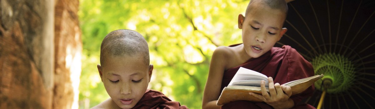 Myanmar little monk reading book outside monastery