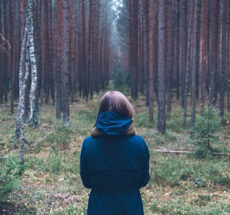 A woman standing before a forest on a cold day.